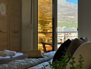 A bedroom with a large window, a bed, a wooden wardrobe, and a view of a mountainous landscape. - Saray Hotel (Bar)