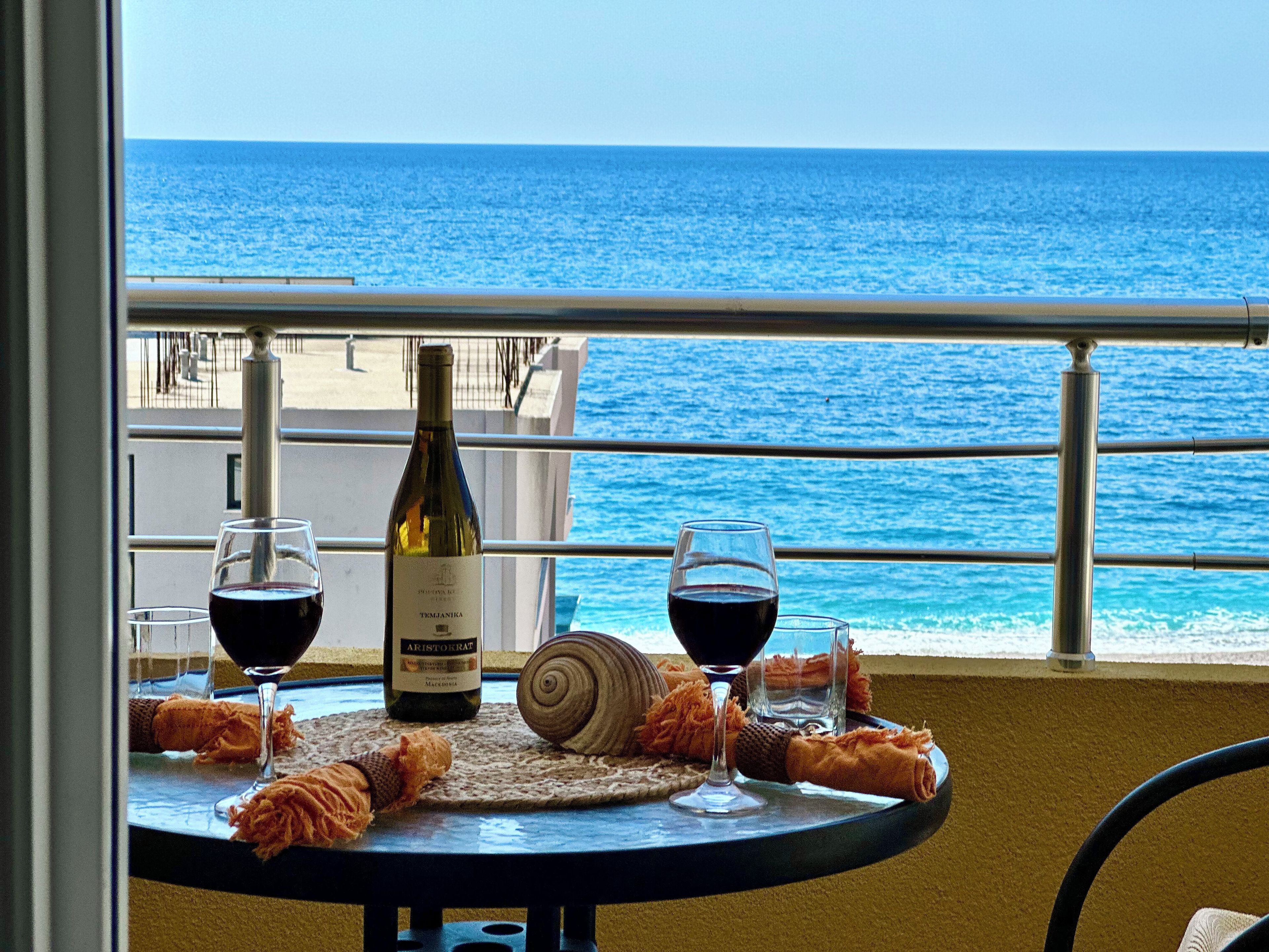 A table with a bottle of wine, two glasses, and a snail on a balcony overlooking the sea.