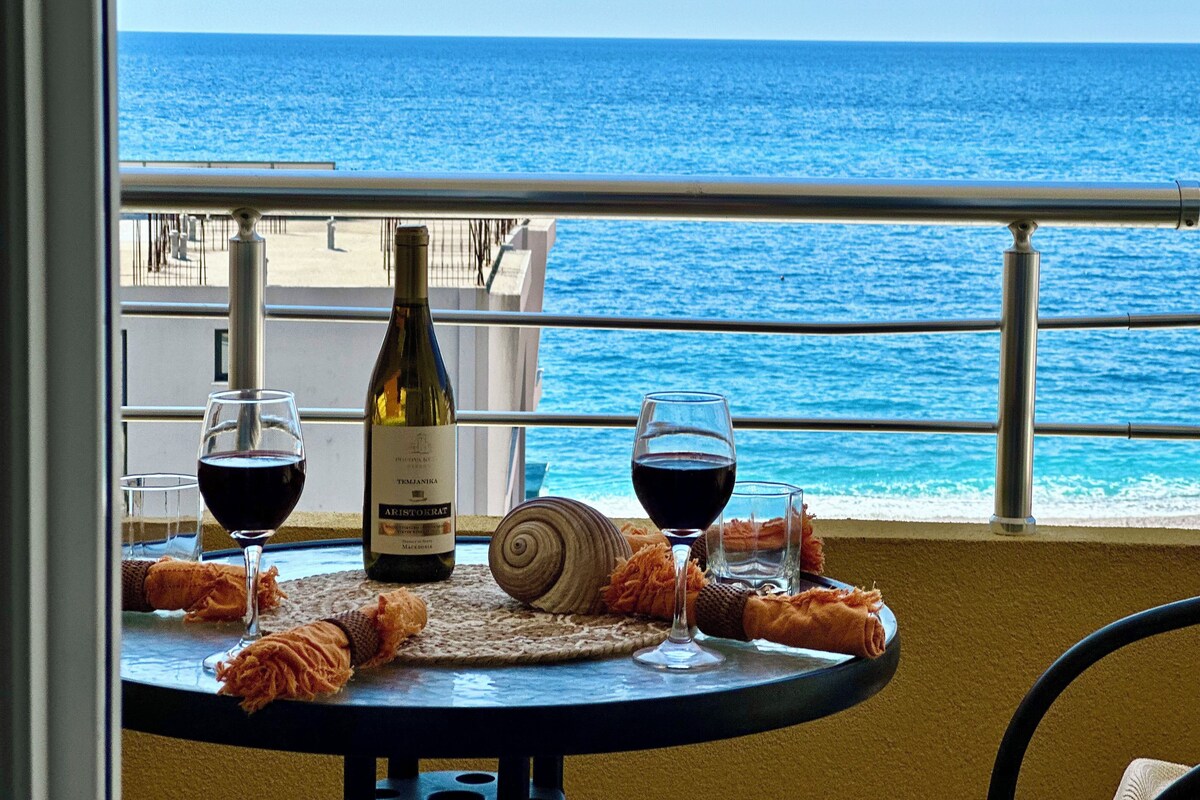 A table with a bottle of wine, two glasses, and a snail on a balcony overlooking the sea.