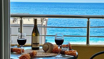 A table with a bottle of wine, two glasses, and a snail on a balcony overlooking the sea.