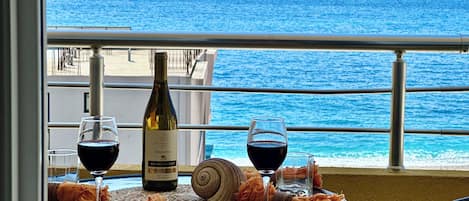 A table with a bottle of wine, two glasses, and a snail on a balcony overlooking the sea.