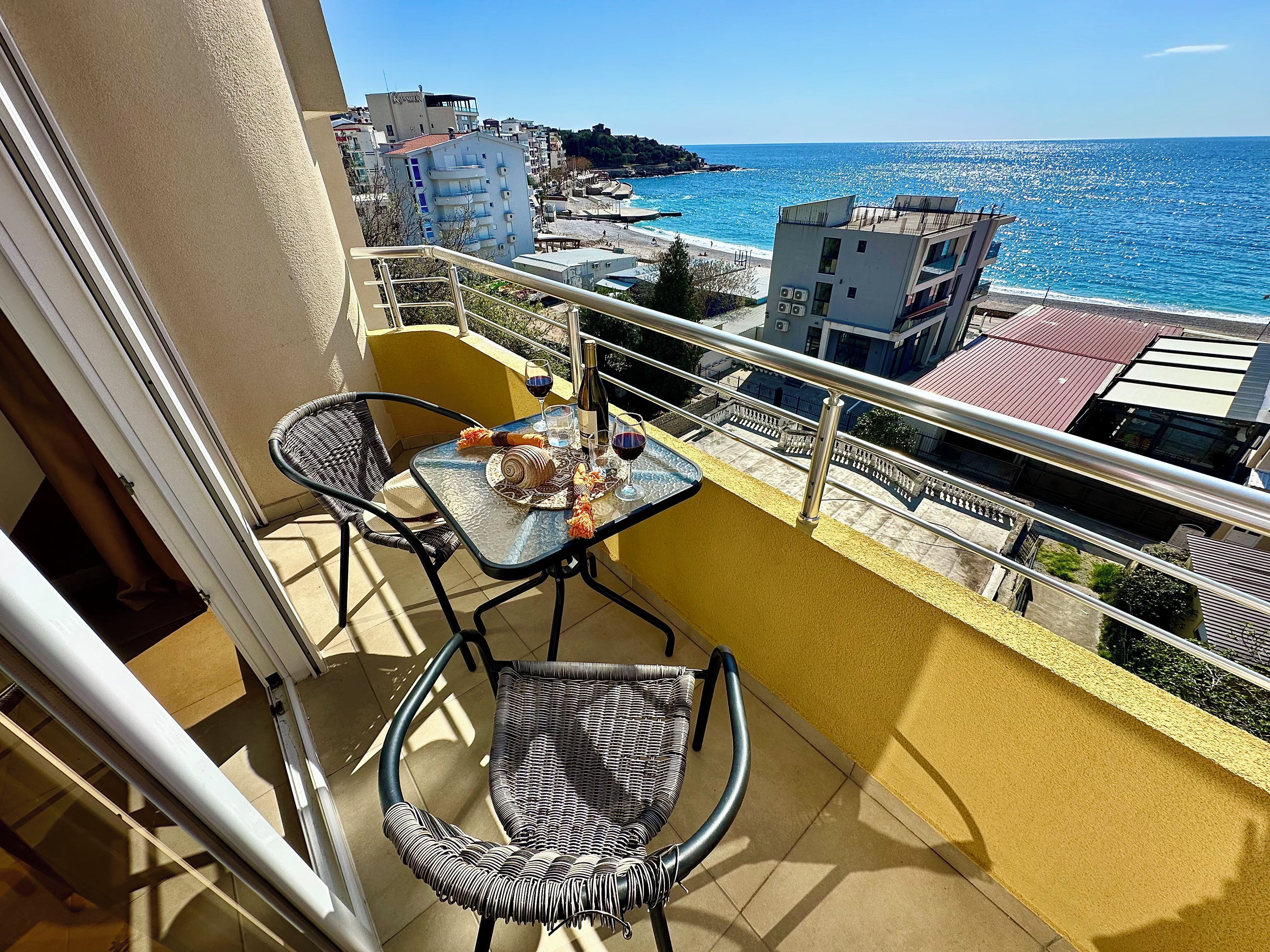 A balcony with a table and chairs, overlooking a beach and buildings.