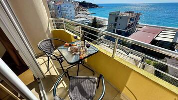 A balcony with a table and chairs, overlooking a beach and buildings.