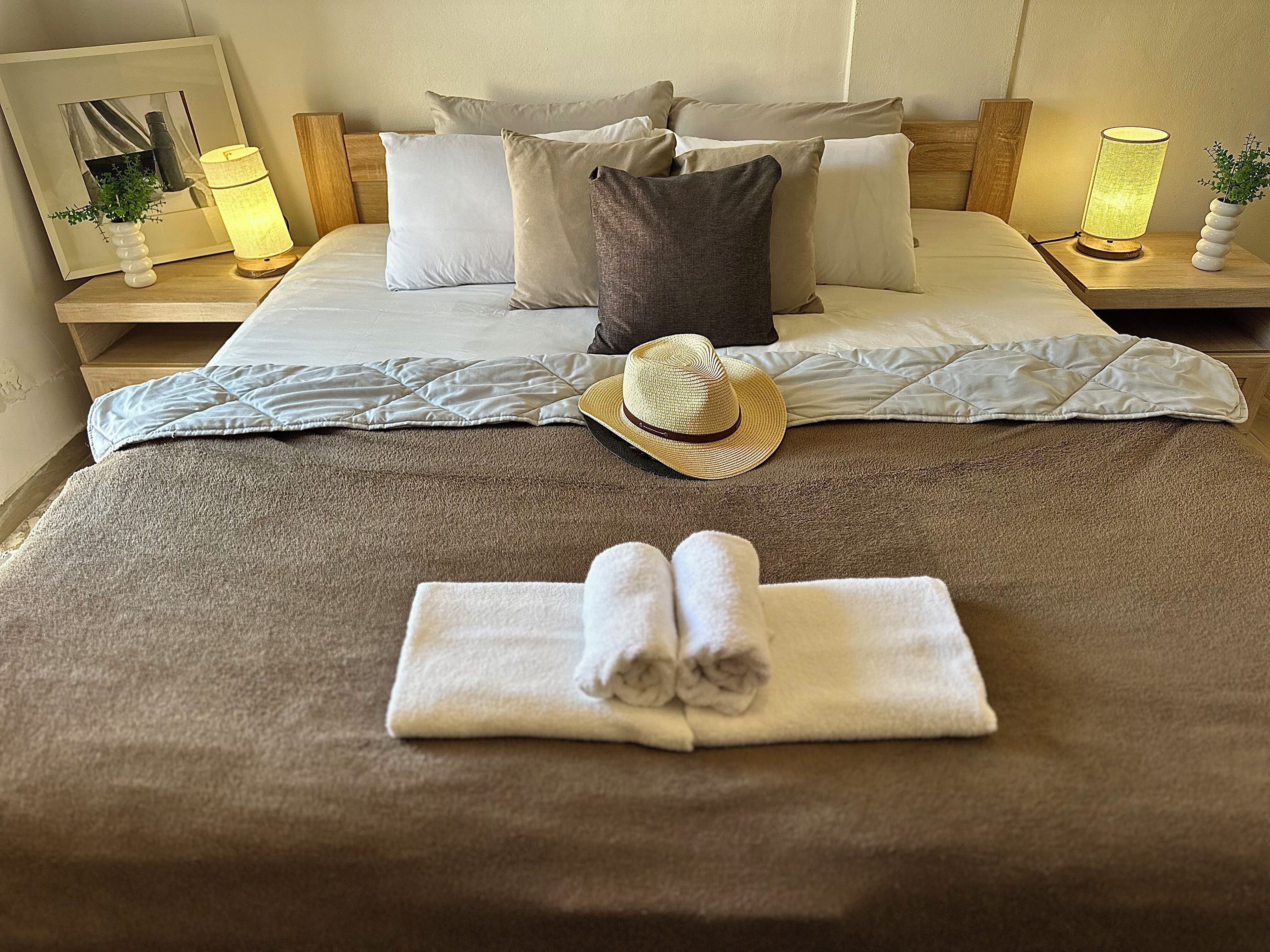 A neatly made bed with pillows, a rolled towel, and a hat on the bed.