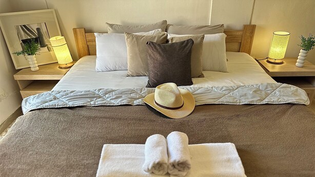 Egy gondosan megterített ágy, rajta párnákkal, egy feltekert törölközővel és egy kalappal.
