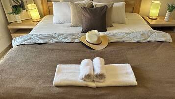 A neatly made bed with pillows, a rolled towel, and a hat on the bed.