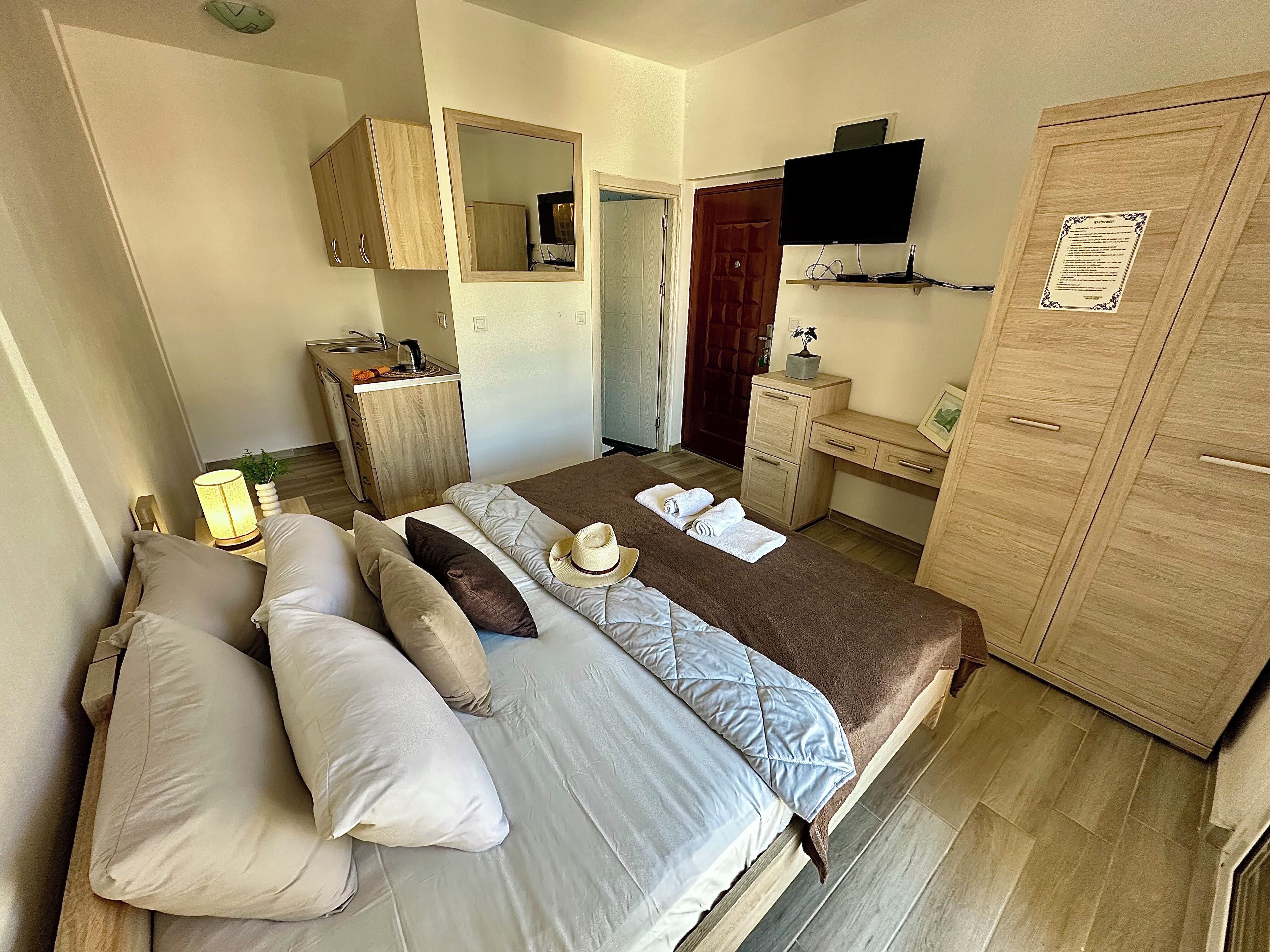 A bedroom with a bed, bedside tables, a wardrobe, a desk, a mirror, and a television.
