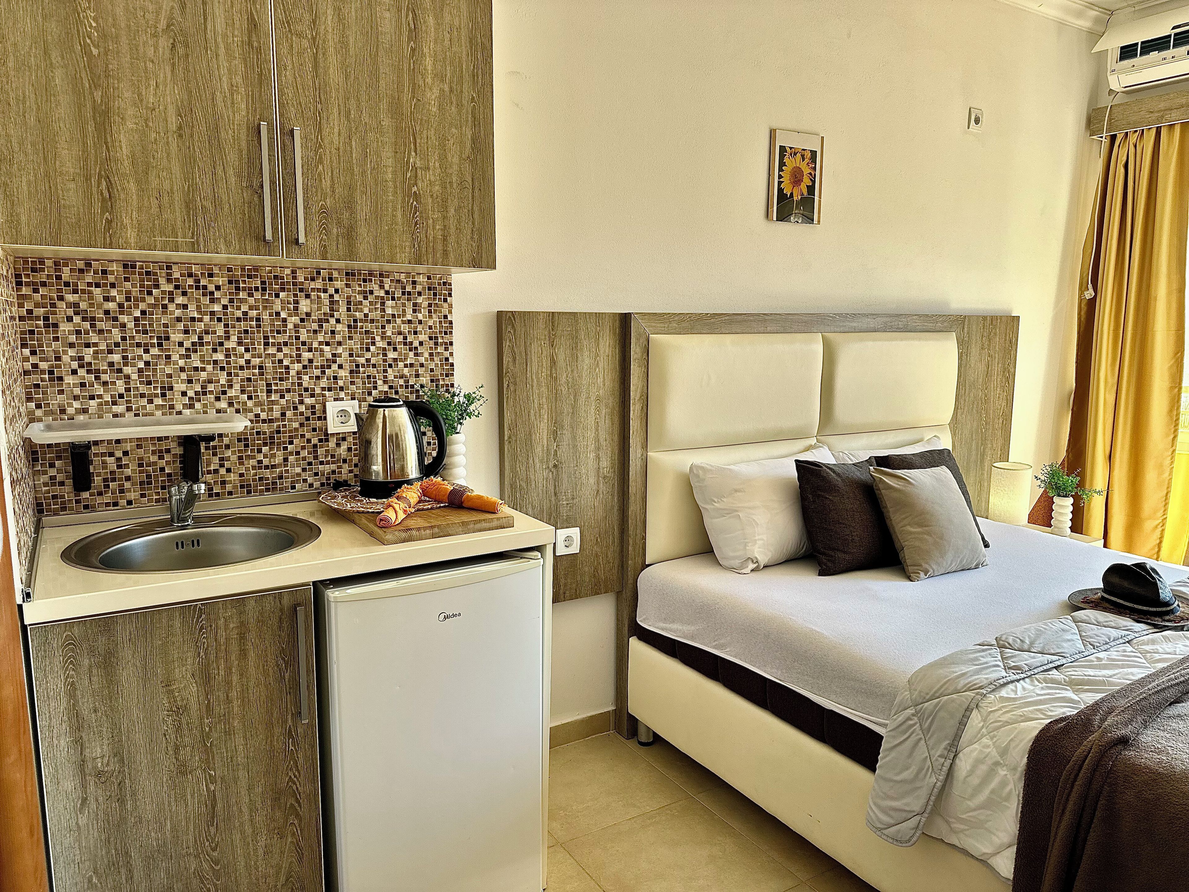 Une chambre d’hôtel compacte comprenant un coin cuisine, un lit avec des oreillers et un petit réfrigérateur.