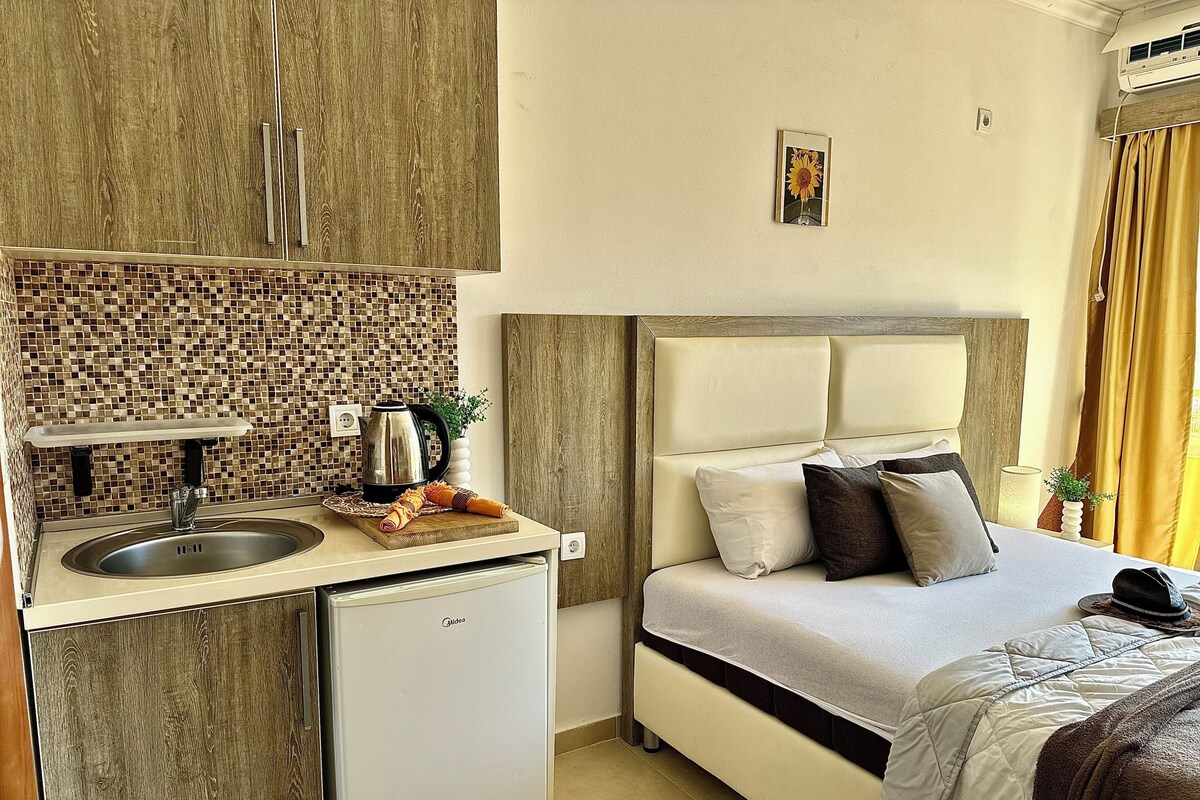 A compact hotel room with a kitchenette, a bed with pillows, and a small refrigerator.
