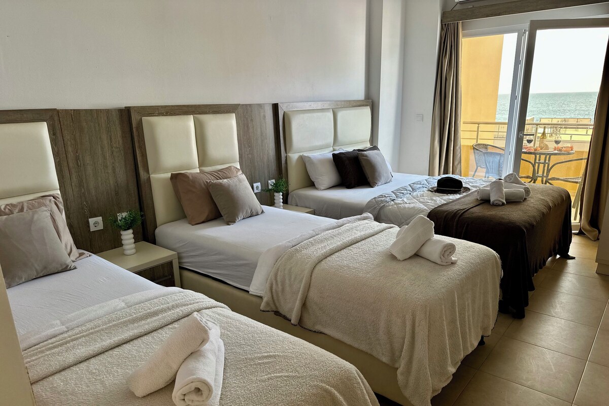 Ein Hotelzimmer mit zwei Betten, einem Balkon mit Meerblick und einem kleinen Tisch mit einer Pflanze.