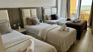 A hotel room with two beds, a balcony with a view of the sea, and a small table with a plant.