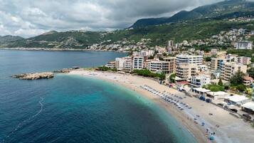 A coastal town with a beach, buildings, and mountains in the background.