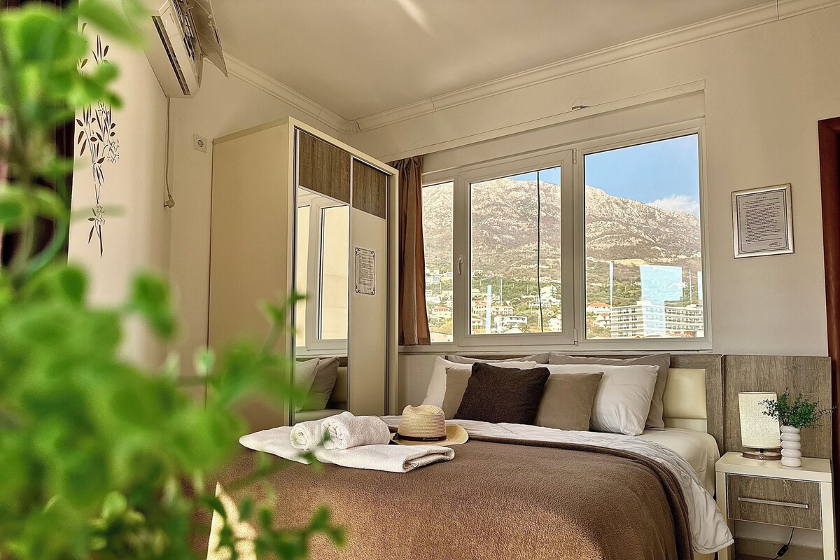 Camera da letto con un letto grande, un comodino con una lampada, una finestra con vista sulle montagne e un condizionatore d'aria a parete.