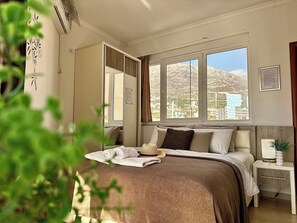 Camera da letto con un letto grande, un comodino con una lampada, una finestra con vista sulle montagne e un condizionatore d'aria a parete.