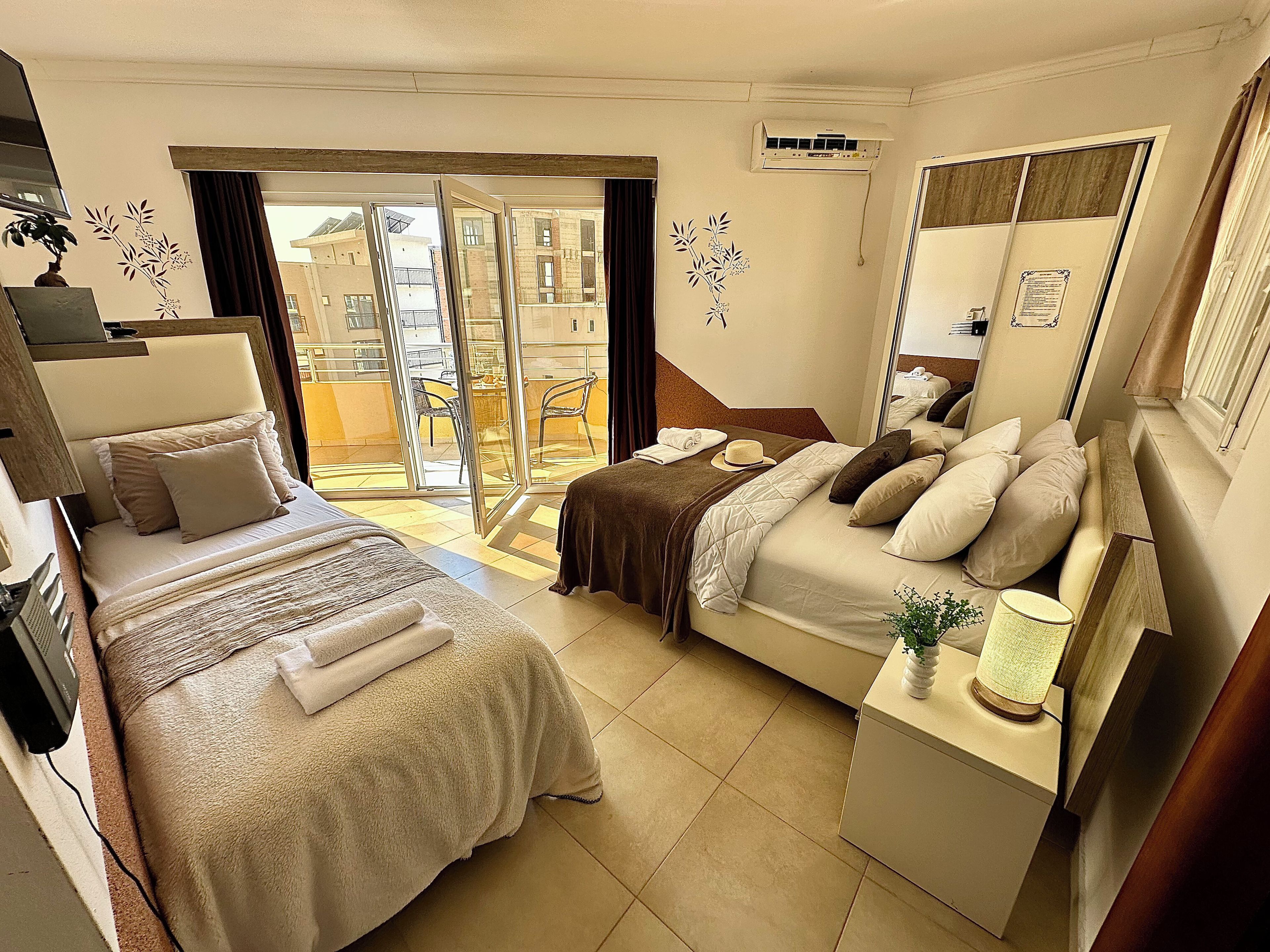 Une chambre d’hôtel avec deux lits, un bureau, une chaise, une petite table avec une lampe et une porte-fenêtre coulissante donnant sur un espace extérieur.