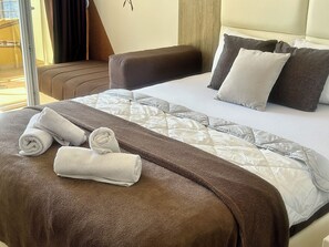 A hotel room with a bed, pillows, a brown sofa, and rolled towels. - Saray Hotel (Bar)