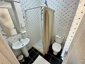 A bathroom with a toilet, sink, shower, and a towel rack. - Saray Hotel (Bar)