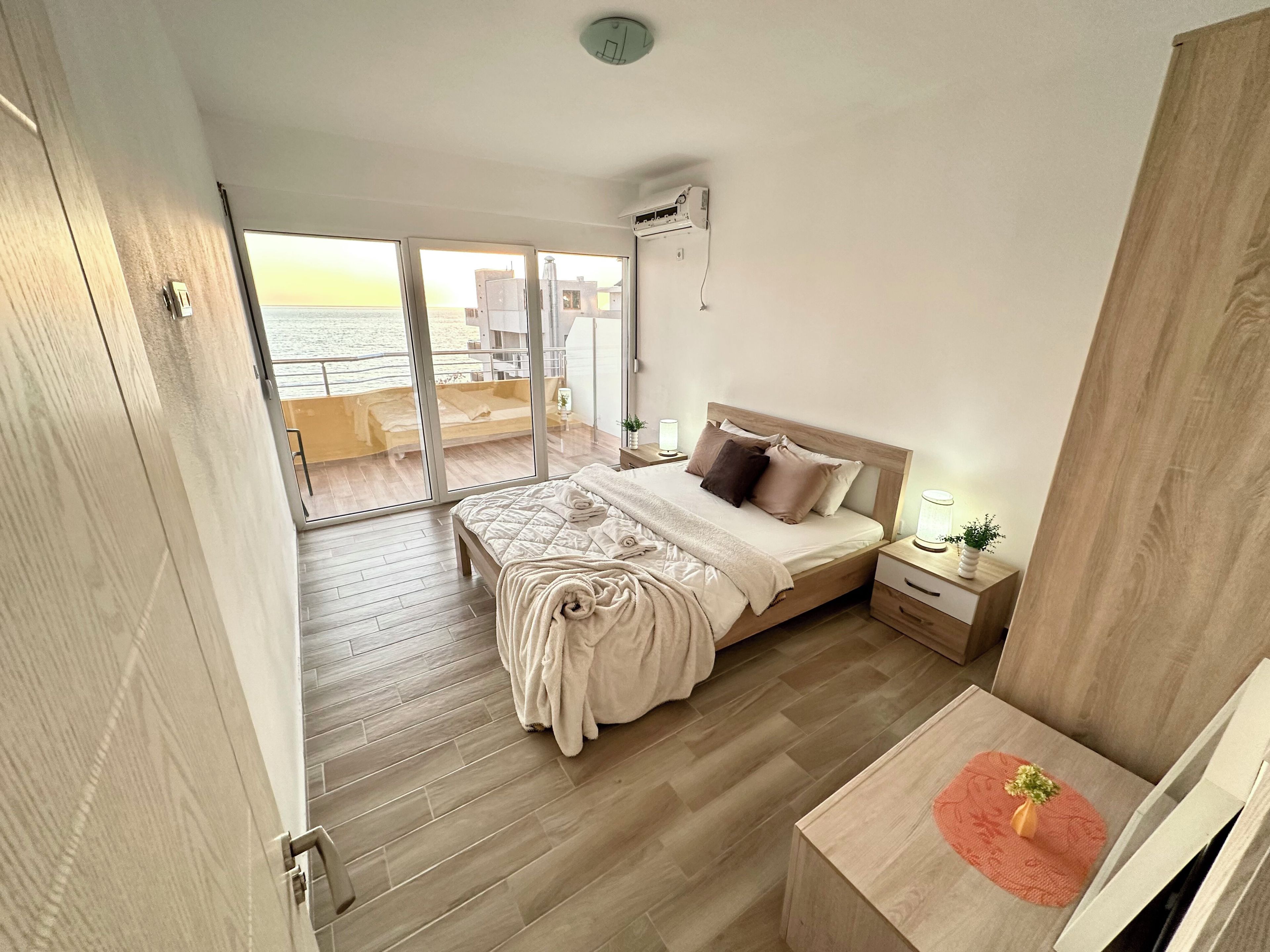 A bedroom with a bed, bedside table, and a view of the sea through a sliding door.