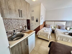 A compact hotel room with a kitchenette, a bed with two pillows, a bedside table with a lamp, and a decorative wall piece. - Saray Hotel (Bar)