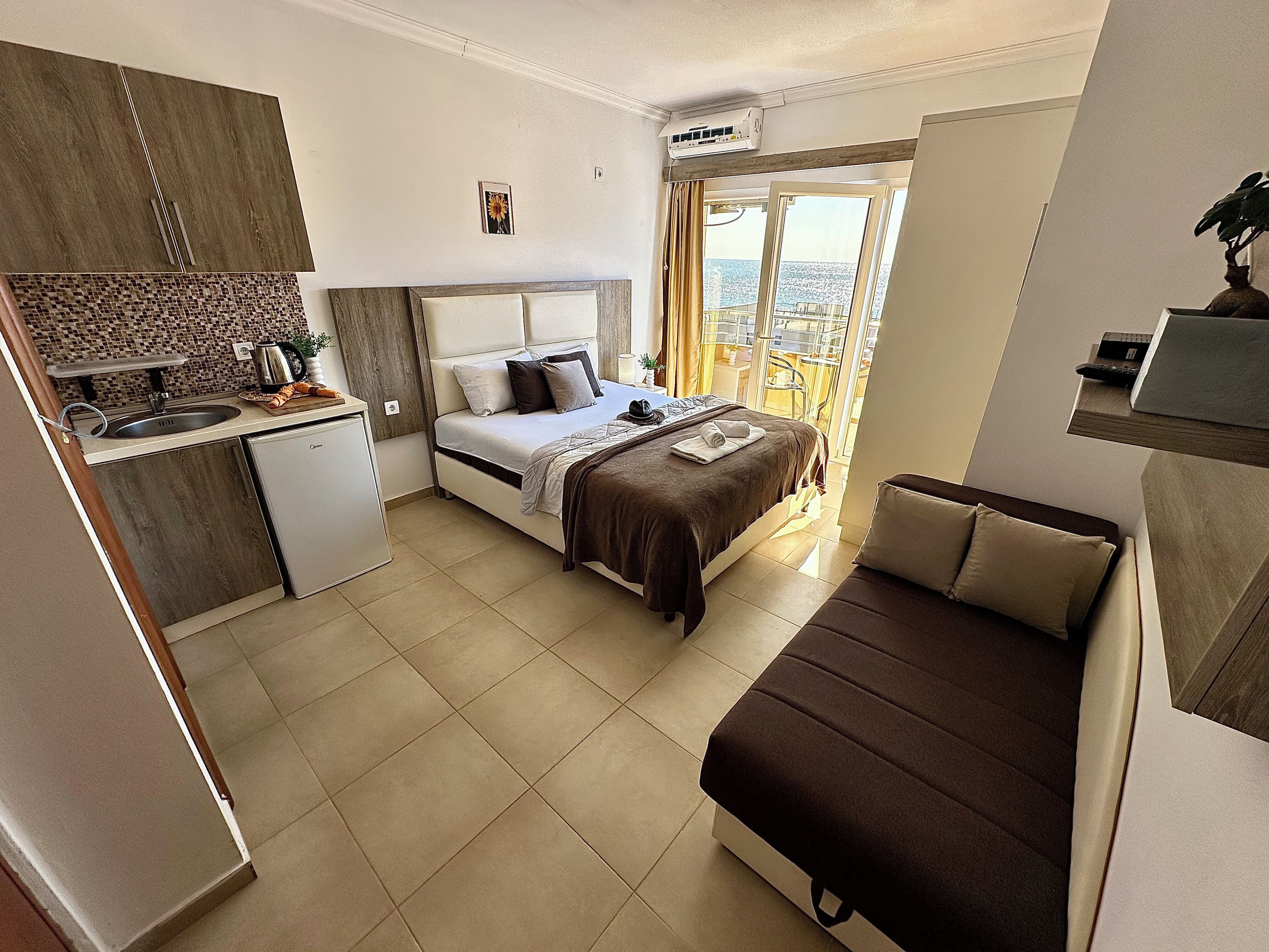 Habitación de hotel compacta con cama, kitchenette y balcón con vistas.