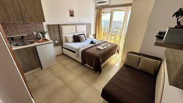 A compact hotel room with a bed, kitchenette, and a balcony with a view.