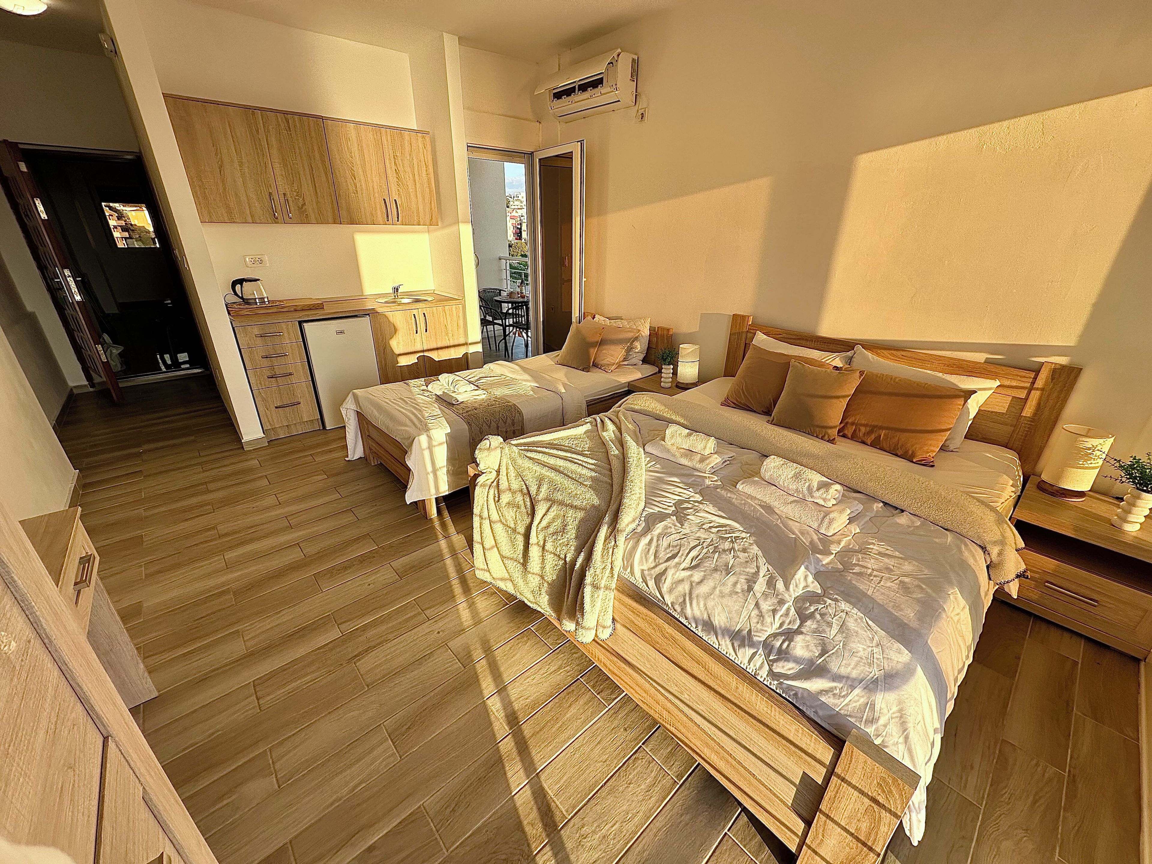 A hotel room with two beds, a kitchenette, a dining area, and a view of the city.