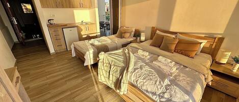 A hotel room with two beds, a kitchenette, a dining area, and a view of the city.