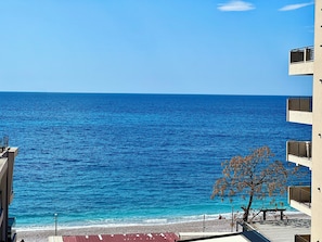 Une vue sur la côte, avec un ciel dégagé, une plage et un bâtiment doté de balcons donnant sur la mer.