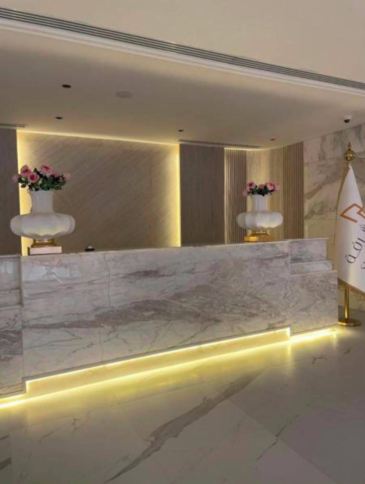 A reception desk with marble top and two vases of flowers, a gold-colored sign with text, and a marble floor.
