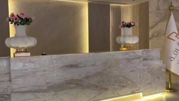 A reception desk with marble top and two vases of flowers, a gold-colored sign with text, and a marble floor.