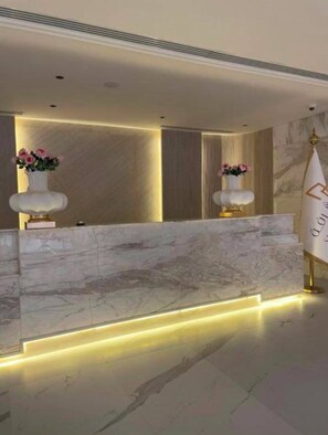 A reception desk with marble top and two vases of flowers, a gold-colored sign with text, and a marble floor. - Shorfa for Hotel Apartments Al-Shorfa (Riyadh)