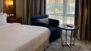 A hotel room with a bed, a chair, a small table, and a window with curtains. - Shorfa for Hotel Apartments Al-Shorfa (Riyadh)