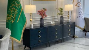 A formal room with a dark blue console table, two lamps, framed portraits, and flags. - Shorfa for Hotel Apartments Al-Shorfa (Riyadh)