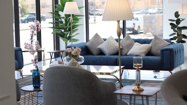 A modern living room with a blue sofa, decorative pillows, a floor lamp, and a vase with flowers. - Shorfa for Hotel Apartments Al-Shorfa (Riyadh)