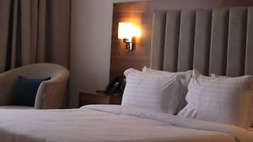 A hotel room with a bed, a chair, a nightstand with a phone, and a wall-mounted lamp.