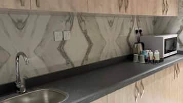 A kitchen with a marble backsplash, wooden cabinets, a stainless steel sink, and a microwave on the countertop.