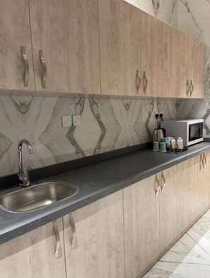 A kitchen with a marble backsplash, wooden cabinets, a stainless steel sink, and a microwave on the countertop. - Shorfa for Hotel Apartments Al-Shorfa (Riyadh)
