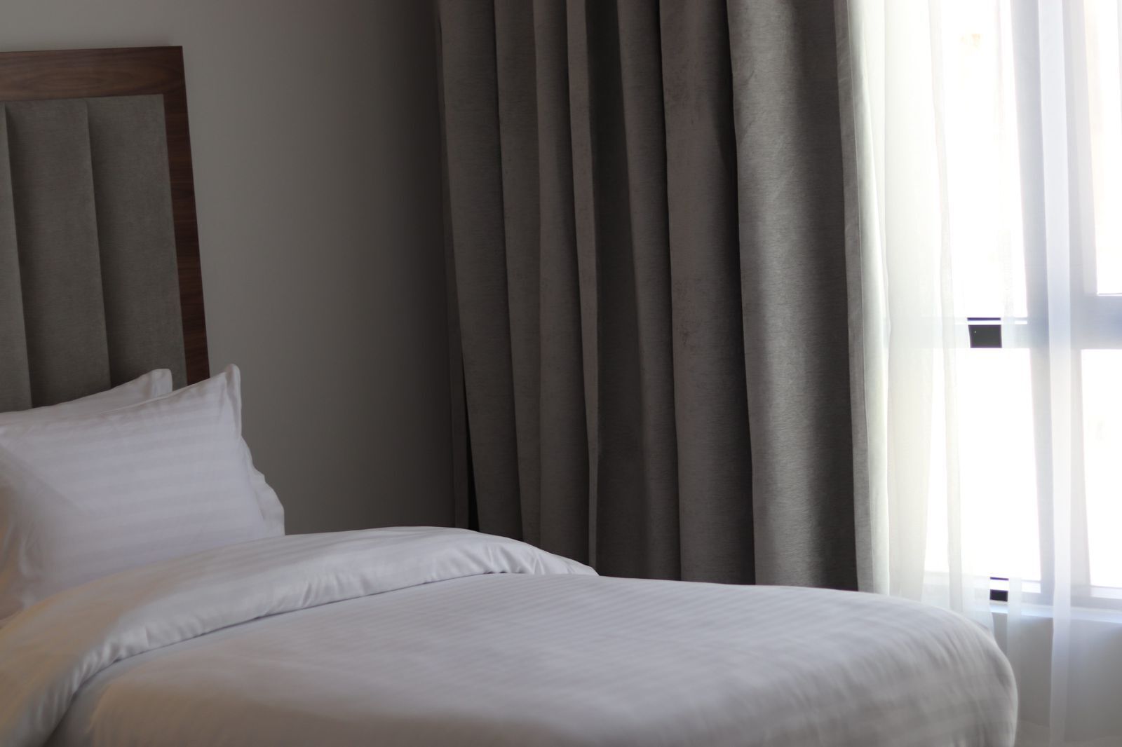 Ett hotellrum med en säng, gardiner och ett fönster.