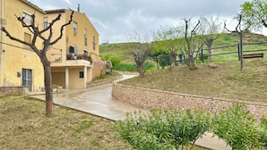 A yellow building with a stone pathway leading to a door, surrounded by greenery and a hilly landscape. - Casa Medieval en el Centro de Montblanc (Montblanc)