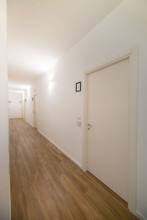 Un couloir avec un plancher en bois, des murs blancs et des portes fermées.