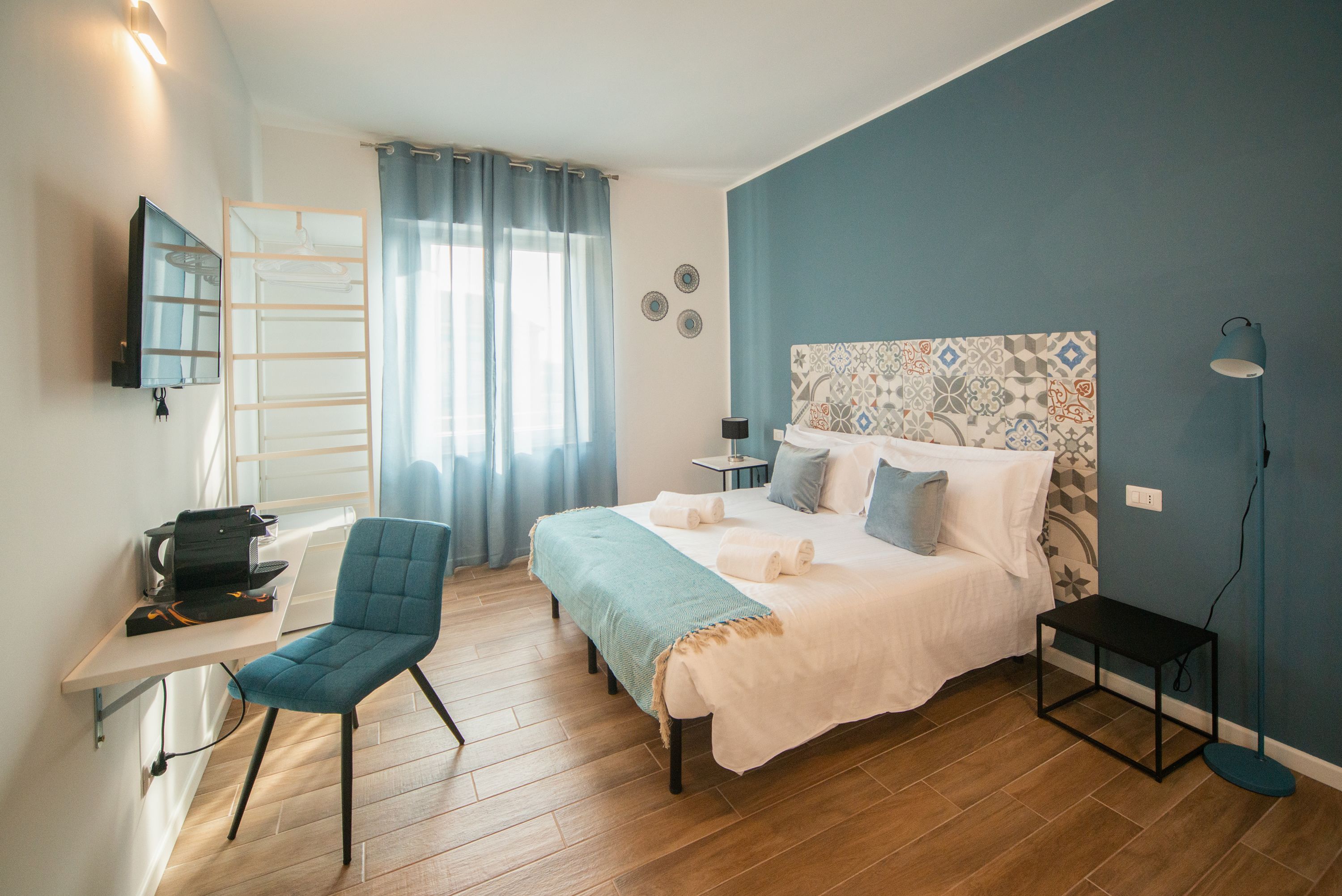 A bedroom with a bed, a desk, a chair, a TV, and a window with curtains.