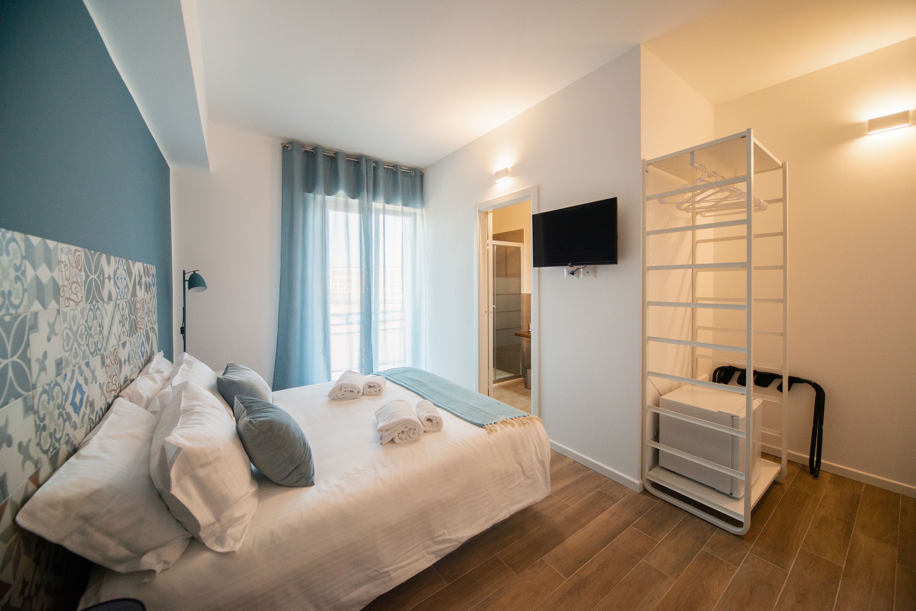A bedroom with a bed, a TV mounted on the wall, a walk-in closet, and a window with curtains.