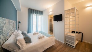 A bedroom with a bed, a TV mounted on the wall, a walk-in closet, and a window with curtains.