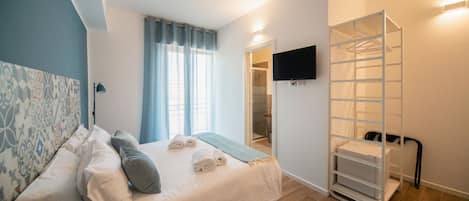 A bedroom with a bed, a TV mounted on the wall, a walk-in closet, and a window with curtains.