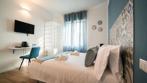 A hotel room with a bed, a desk with a chair, a TV mounted on the wall, and a window with curtains. - Casa Stazione (Verona)