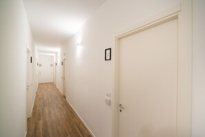 A narrow hallway with wooden flooring and white walls, leading to a closed door marked with the number 1. - Casa Stazione (Verona)