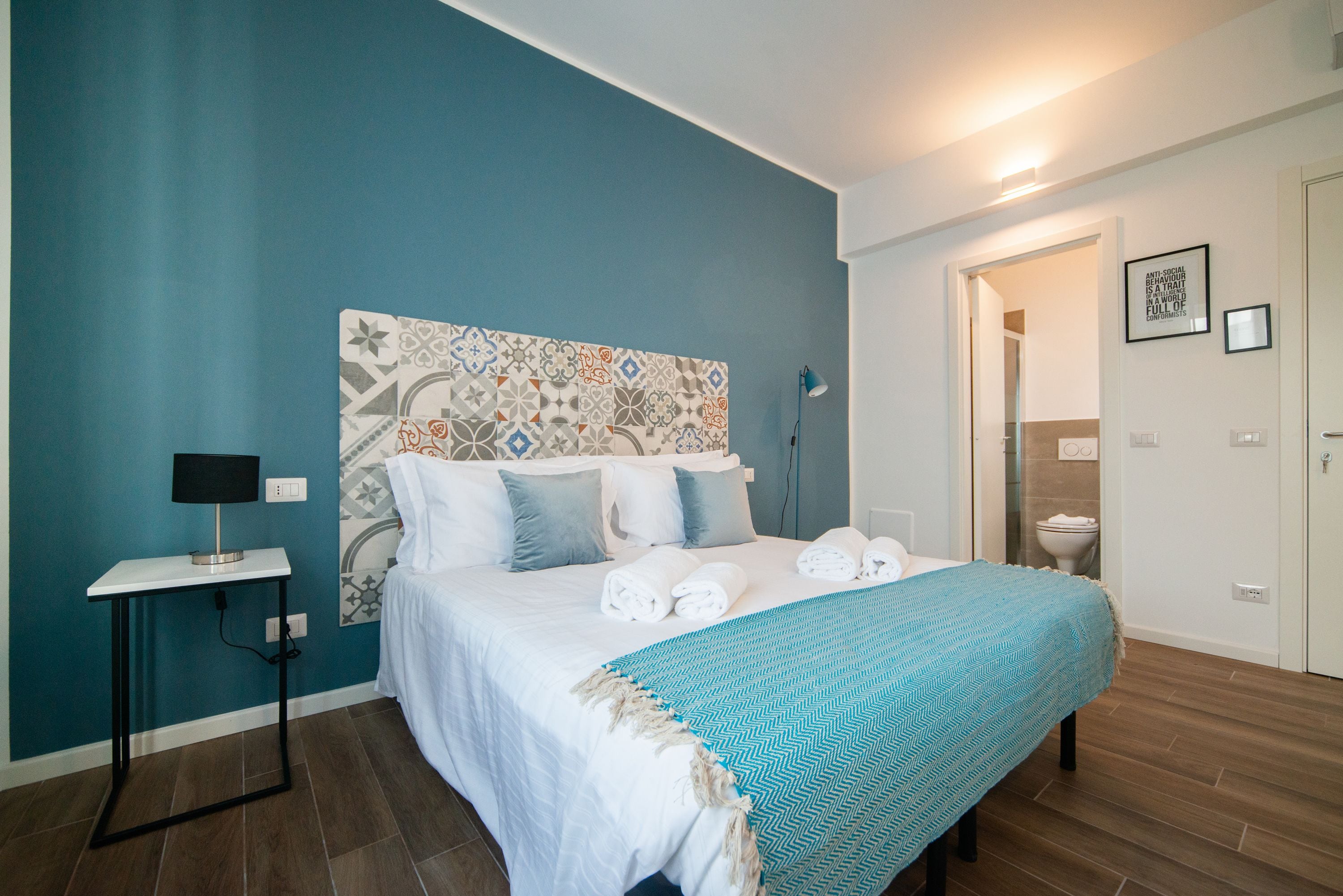 A bedroom with a bed, a bedside table with a lamp, and a wall with a patterned headboard.