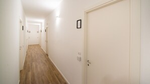 A narrow hallway with wooden flooring and white walls, leading to a closed door marked with the number 1. - Casa Stazione (Verona)