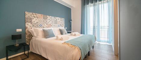 A bedroom with a large bed, a bedside table, a lamp, and a window with curtains.
