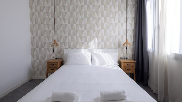 A neatly made bed with two towels, a geometric patterned wall, and two bedside lamps. - Stay U-nique Apartments at Av. Republica Argentina (Barcelona)